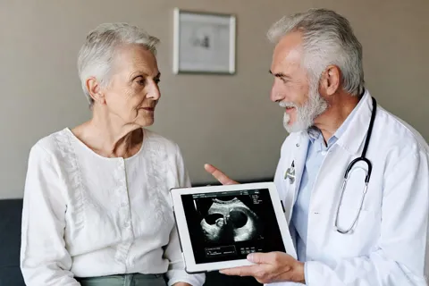 Médico explicando resultado de ultrasonido abdominal a un paciente mayor, en un entorno clínico tranquilo.