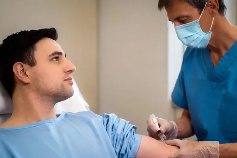 Persona sentada en una clínica mientras una enfermera toma una muestra de sangre de su brazo para analizar sus niveles de lipoproteína(a).