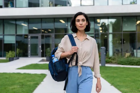 Persona caminando con confianza hacia un edificio de oficinas, con una mochila y una botella de agua, simbolizando un regreso seguro y empoderado al trabajo tras un evento cardíaco.